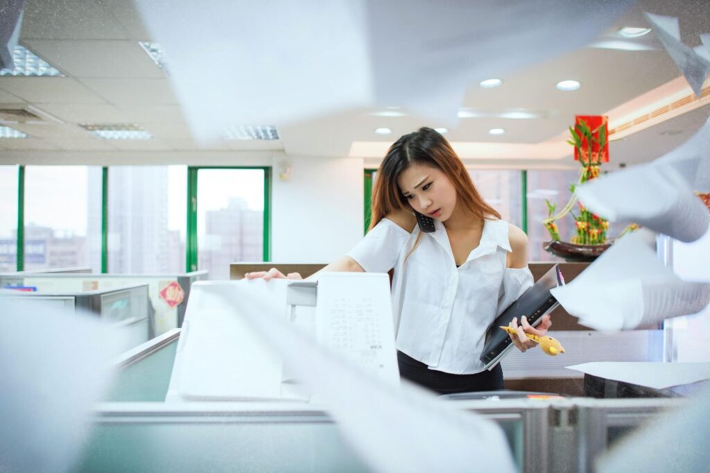 採用担当者が多忙で手が回らず、面接結果の連絡が遅れてしまう状況を表すイメージ。電話対応と大量の書類処理に追われる人事担当者